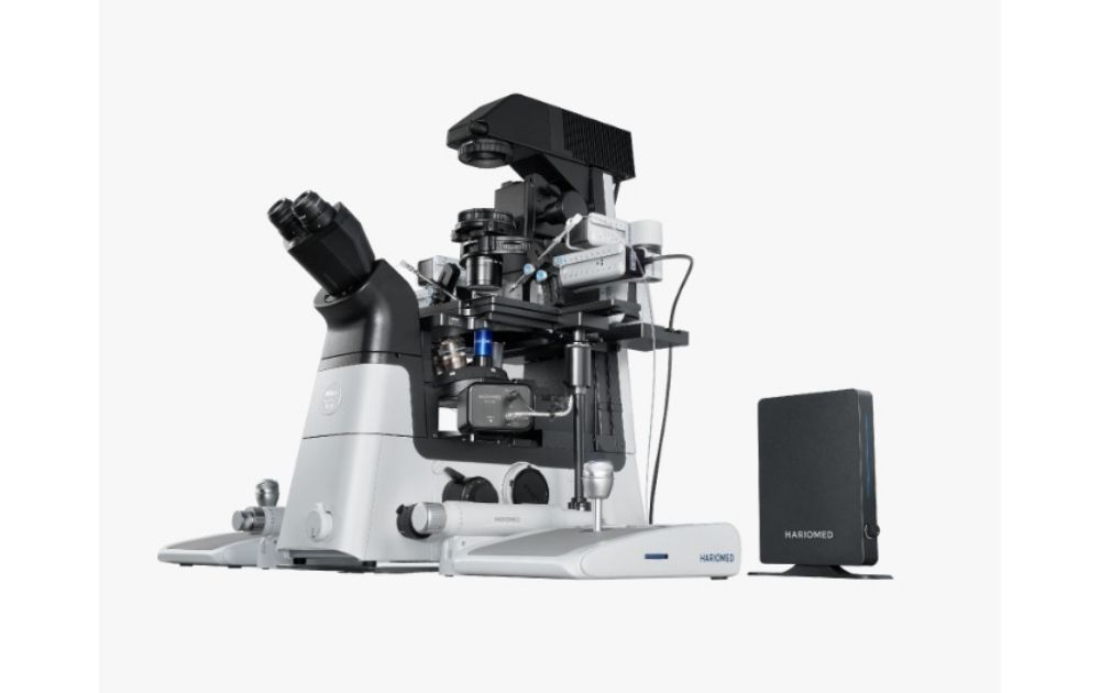 Microscopio de laboratorio avanzado marca Haromed, de color blanco y negro, sobre un fondo blanco. El equipo de investigación científica se muestra junto a su unidad de control externa.